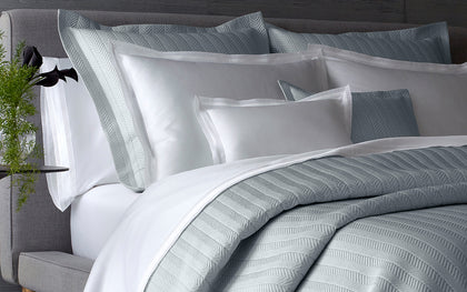 Gray herringbone-quilted Netto bedding layered on a bed with white pillows.