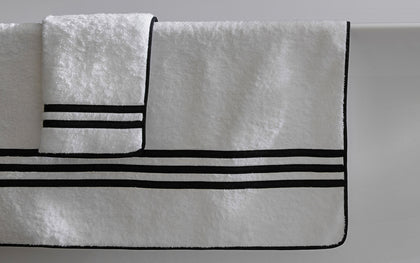 White Newport towels with black striped borders draped over a tub edge.