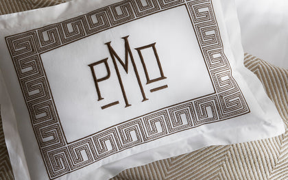 White Ophelia pillow with monogrammed brown Greek key border styled on herringbone bedding.
