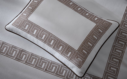 White Ophelia Pique pillow sham with brown Greek key border on textured bedding.