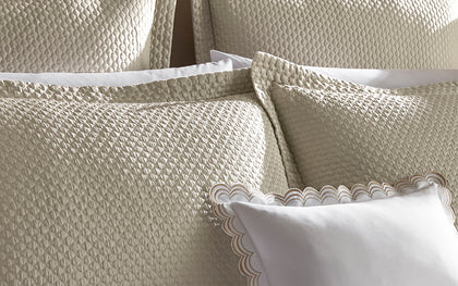 Textured cream Perla shams layered with a white scalloped-trim pillow.