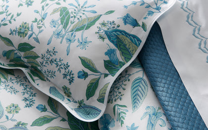 White Pomegranate floral-print pillow sham with blue and green botanicals beside a quilted blue throw.