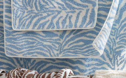 Blue zebra-print Regine towel stacked beside brown and taupe towels.
