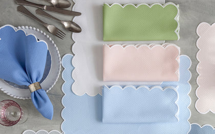 Scalloped-edge Savannah Gardens placemats and folded napkins in green, pink, and blue beside place settings.