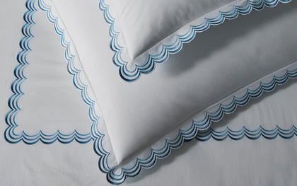 White Stella bedding with blue scalloped embroidered trim layered on a bed.