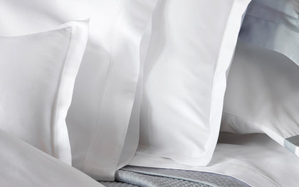 White Talita Satin Stitch pillow shams layered with blue-trimmed pillows.