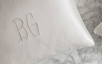 White monogrammed silk pillowcase from The Silk Collection on a marble surface.