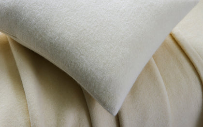 Cream Venus wool blanket and pillow draped on a bed.