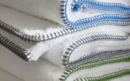 White Whipstitch towels with blue, gray, and green whipstitch trim stacked together.