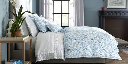 Blue Alexandra floral print bedding styled on a bed near a large window.