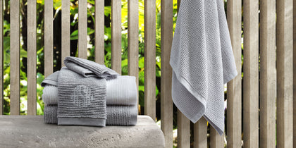 Gray ribbed Aman towels, monogrammed, stacked and hanging on an outdoor slatted fence.