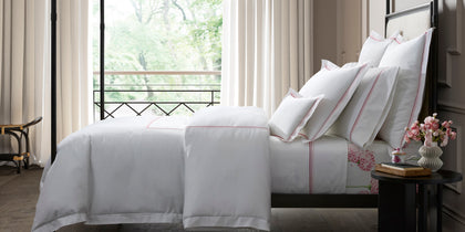 White Amara Triple Pearl bedding with red dot-embroidered trim, styled on a bed near a balcony window.