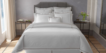White Ambrose bedding with satin bordered trim, styled on a bed with monogrammed shams.