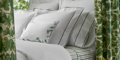 White Ansonia bedding with green single-stripe trim, styled on a bed with a leaf-print headboard.