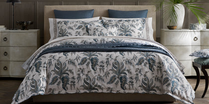 Blue Apolline floral print bedding styled on a bed with navy quilted pillows.