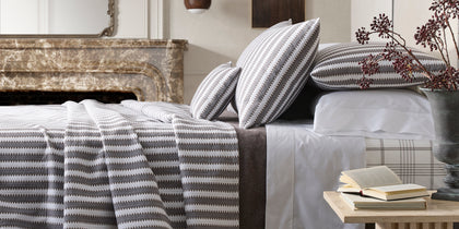Gray and white Apollo Stripe Matelasse quilted bedding styled on a bed near a marble fireplace.