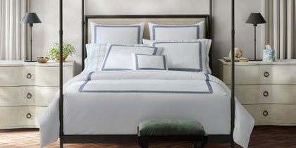 White Astor Braid bedding with navy loop-embroidered trim, styled on a bed with a four-poster frame.