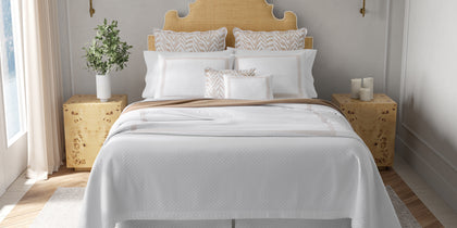 White Astor Braid quilted bedding with tan zebra-print pillows, styled on a bed with a rattan headboard.