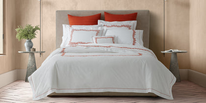 White Atoll bedding with coral embroidered border, styled on a bed with rust-colored pillows.