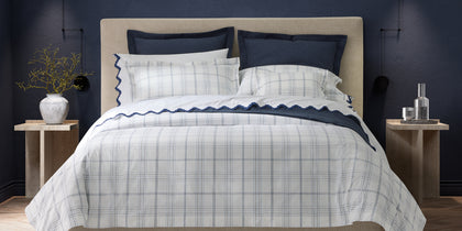 White and navy August Plaid bedding with scalloped trim, styled on a bed against a navy wall.