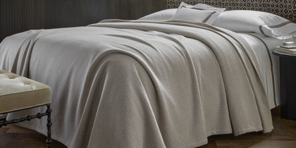 Tan Avalon herringbone-woven blanket draped over a bed with white sheets.