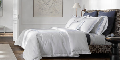 White Axel bedding with wavy embroidered trim, styled on a bed with navy pillows.