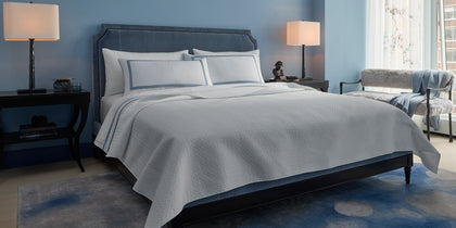 White Basketweave quilted bedding styled on a bed with a blue velvet headboard.