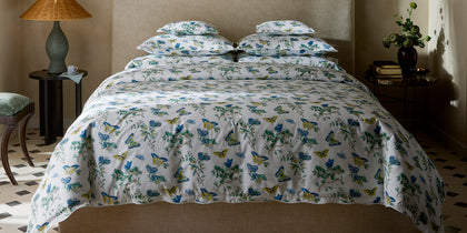 White Baudin Butterfly bedding with a blue, green, and yellow butterfly print, styled on a bed with a tan headboard.