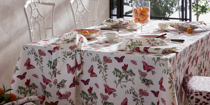 Baudin Butterfly print tablecloth set with bamboo chairs and teacups near a window.