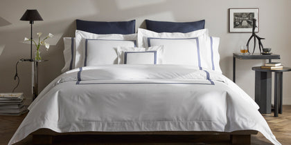 White Bel Tempo bedding with navy stripe trim, styled on a bed with navy accent pillows.