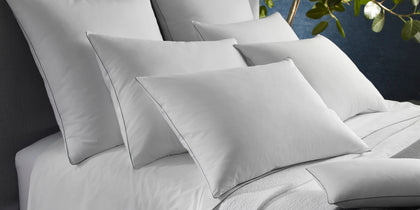 White Bryant shams with dark piped edging, stacked on a bed near greenery.
