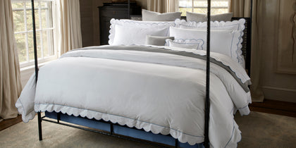 White Butterfield scalloped bedding with blue trim, styled on a four-poster bed.