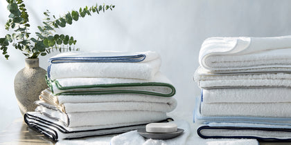 White Cairo towels with navy, green, and black piping stacked beside a soap dish