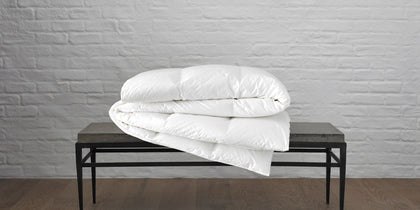 Chalet white down comforter folded on a bench against a brick wall