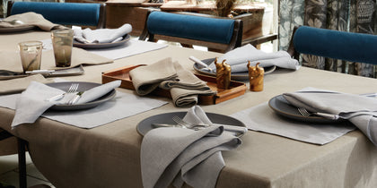 Tan Chamant linen tablecloth set with gray napkins on a table with blue upholstered chairs.