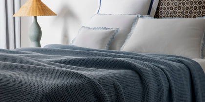 Navy waffle-weave Chatham blanket draped on a bed with scalloped blue-trimmed shams.