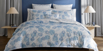 Blue Chrysanthemum print bedding styled on a bed against a blue wall.
