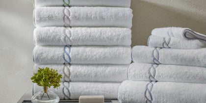 White Classic Chain towels stacked with chain-link trim in assorted colors, beside soap and a plant.
