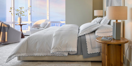 White Classic Chain Scallop bedding with gray chain-embroidered trim, styled on a bed near a city window.