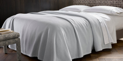 Light gray Costa Mesa textured blanket draped over a bed with white sheets.