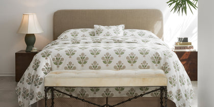 Green Dalila floral print bedding styled on a bed with a tan upholstered headboard.