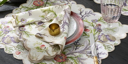 Del Tesoro coral and shell print scalloped placemat set with a pink plate and glassware.