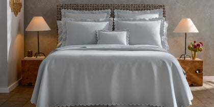 Pale blue Diamond Pique scalloped bedding styled on a bed with a patterned headboard.