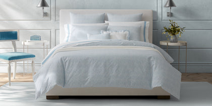Pale blue Duma Diamond print bedding styled on a white upholstered bed.