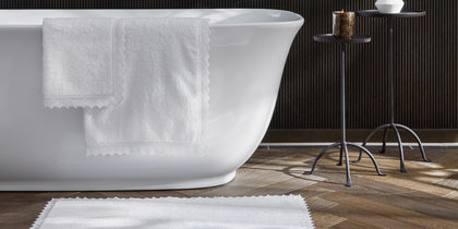 Ellis white lace-trim towel and bath mat by a freestanding tub