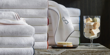 White Giza towels stacked with colorful trim, styled on a marble shelf with soaps.