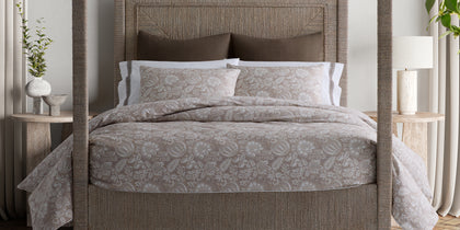 Tan Granada floral print bedding, styled on a woven four-poster bed.