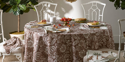 Brown Granada floral print tablecloth set for outdoor dining with bamboo-style chairs and a Tiger Palm napkin.