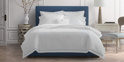 White Hatch bedding with cross-stitch trim, styled on a bed with a navy upholstered headboard.