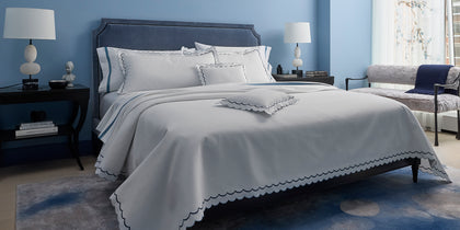 White India Pique scalloped bedding with navy trim, styled on a bed against a blue wall.